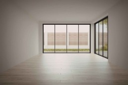 A large empty off-white room with large windows with black frames and wooden floors.